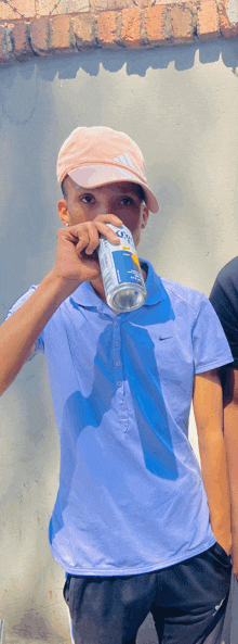 a young man wearing a nike polo shirt is drinking from a can