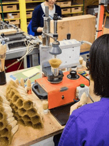 a woman is sitting at a table making brushes in a factory .