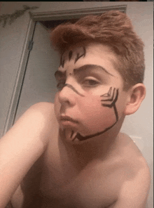 a shirtless boy with a drawing on his face looks at the camera