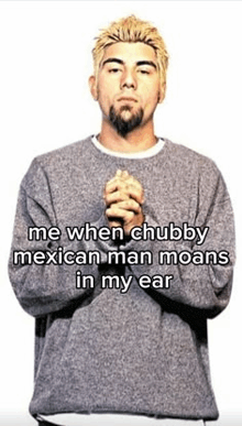 a man with a beard and a gray sweater is standing with his hands folded in front of his face .