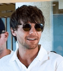 a man wearing sunglasses and a white shirt is smiling