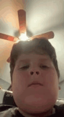 a young boy is taking a selfie with a ceiling fan behind him .