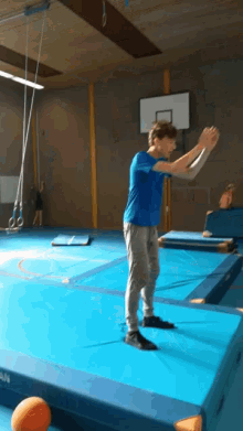 a man in a blue shirt stands on a blue mat in a gym with a basketball in the background