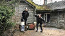 two men are standing in front of a wooden house