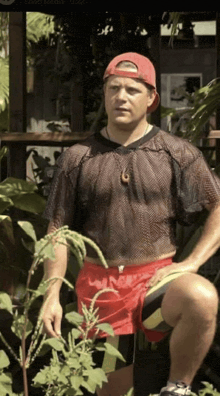 a man wearing a red hat and a black shirt is standing in a garden