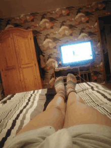 a person laying on a bed with their feet crossed in front of a television