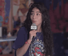 a woman is talking into a microphone while wearing a raptors t-shirt .