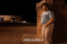 a man with a mustache is standing next to a wall with the name josh garcia written on the bottom .