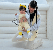 a woman is kneeling down holding a baby and the baby is wearing yellow adidas shoes