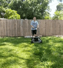 a man is using a lawn mower in front of a wooden fence with a shirt that says rays on it