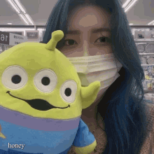 a woman wearing a mask holds a stuffed toy that has the word honey on it