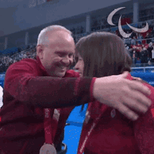 a man and woman are hugging and the woman is wearing a red jacket with the canadian flag on it