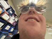 a man wearing glasses is smiling in front of a stack of blue bins with one labeled ' pink frog '