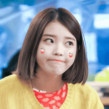 a girl with a sticker of a strawberry on her cheek is wearing a yellow sweater