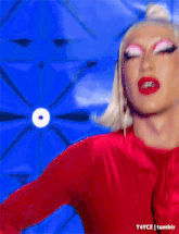a drag queen is wearing a red dress and dancing on a blue background .