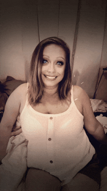 a woman in a white tank top is smiling and looking at the camera