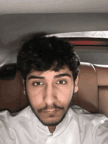 a young man with a beard is sitting in the back seat of a car and taking a selfie .