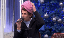 a man with a towel wrapped around his head singing into a microphone in front of a christmas tree