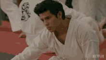 a man in a white karate uniform sits on a red mat with netflix written on the bottom right