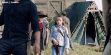 a group of children are walking in a field with a man in a cowboy hat in the background .