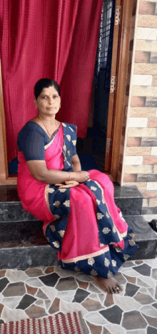 a woman in a pink and blue saree is sitting on a tiled floor in front of a door .