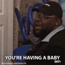 a man wearing a hat and glasses says " you 're having a baby "