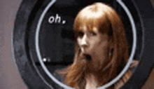 a woman with red hair is yawning while looking through a hole in a mirror .