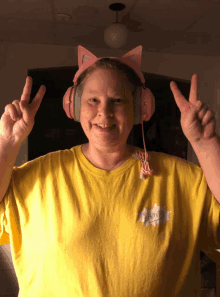 a woman wearing pink headphones and a yellow shirt with a cartoon character on it giving a peace sign