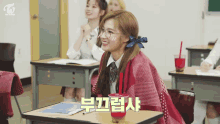 a girl wearing glasses sits at a desk in a classroom with the word twice on the bottom right