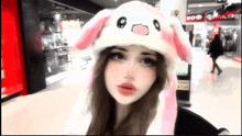 a woman wearing a pink and white bunny hat stands in front of a kfc sign