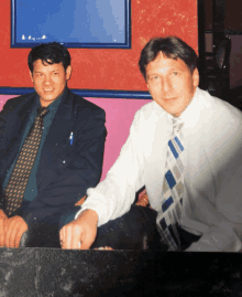 a man in a suit and tie is sitting next to another man