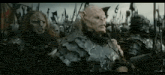 a group of orcs are standing next to each other in a field holding spears .