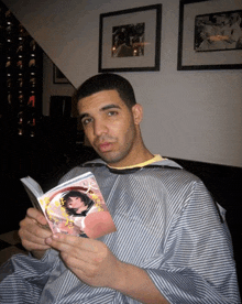 a man wearing a striped shirt is reading a book with a picture of a woman on the cover