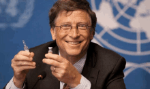 bill gates smiles while holding a small bottle in his hands