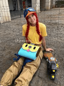 a woman in a costume is sitting on the ground next to a fence holding a bag .