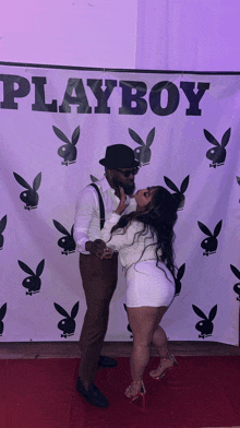 a man and a woman pose in front of a playboy banner