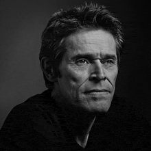 a black and white photo of a man wearing a black shirt and looking at the camera .