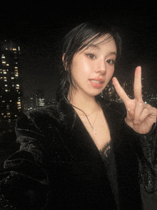 a woman wearing a black jacket and necklace giving a peace sign