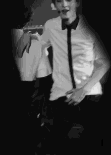 a black and white photo of a man in a white shirt and tie dancing on a stage .