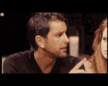 a man in a black shirt talks to a woman in a dark room