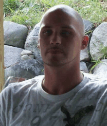 a man with a shaved head and a beard is sitting in front of rocks .