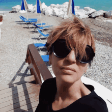 a woman wearing sunglasses and a black shirt is standing on a beach