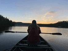 a woman sits in a canoe on a lake with a paddle