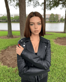 a woman wearing a black leather jacket stands in front of a body of water