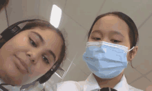 two girls wearing face masks and headphones looking at the camera