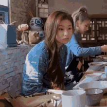 two women are sitting at a table with bowls of food . one of the women is looking at the camera .