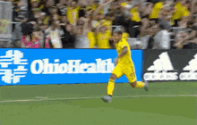 a man in a yellow jersey is running on a soccer field in front of an ohio health sign .