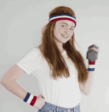 a woman with red hair wearing a headband and wristbands is holding a dumbbell