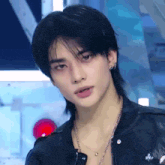 a young man with long black hair and a mullet hairstyle is wearing a leather jacket and a necklace .