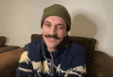 a man with a mustache wearing a green hat and a blue sweater